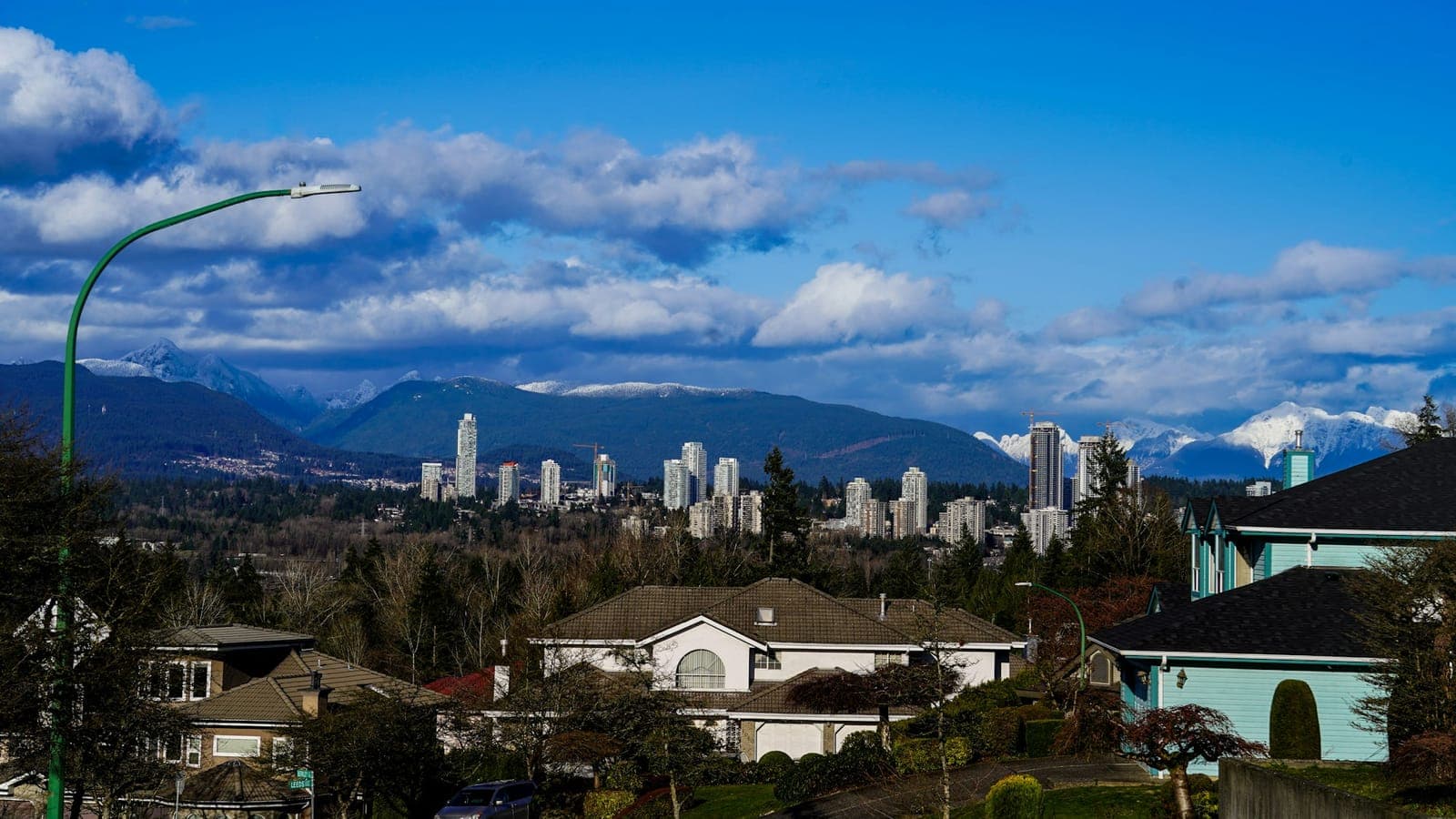 Suburban homes with town-centre towers and snow-capped mountains behind on a sunny day